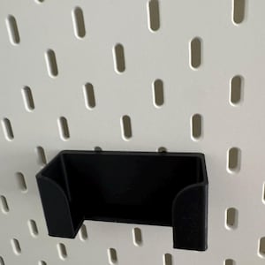 Pu&ograve; includere: Porta telefono in plastica nera montato su una parete in pannello forato bianco.