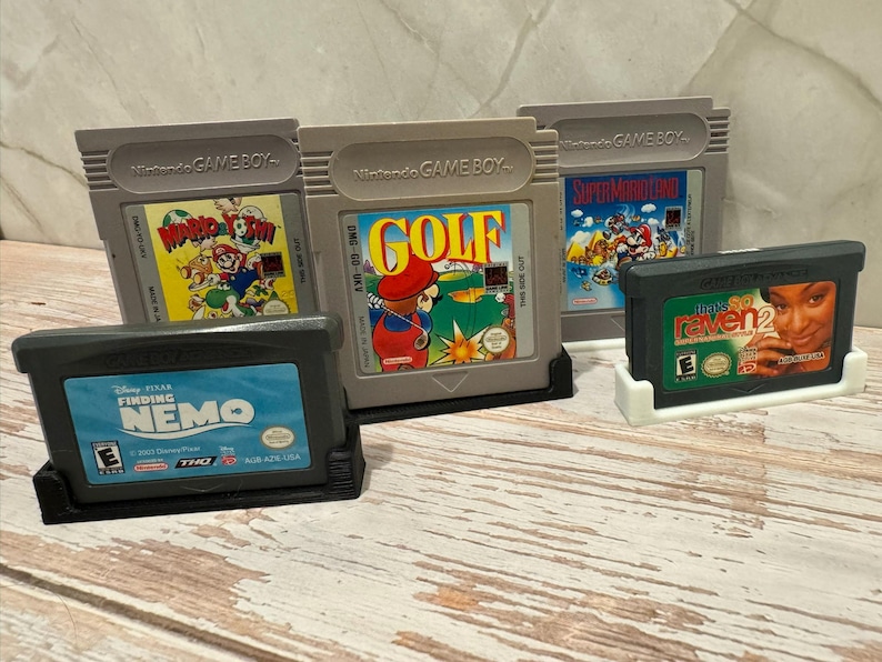 May include: A collection of video game cartridges for Nintendo Game Boy and Game Boy Advance. Games include "Wario Land", "Golf", "Super Mario Land", "Finding Nemo", and "Raven 2". The cartridges are in gray and black plastic.