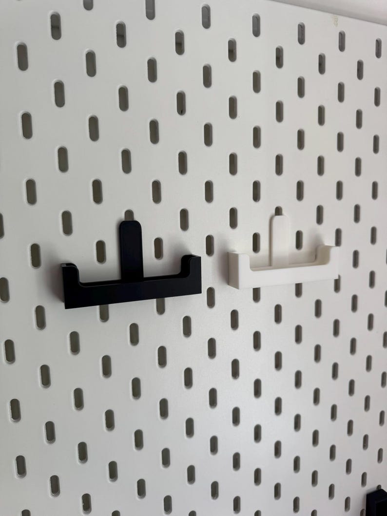May include: A white pegboard with evenly spaced oval holes. Two shelf brackets are attached. One bracket is black, the other is white. The brackets are designed to hold shelves or other accessories. The pegboard provides a versatile storage solution.