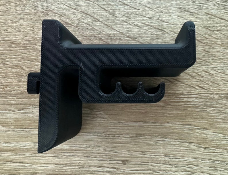 Pu&ograve; includere: Un supporto per cuffie nero stampato in 3D. Il supporto ha una base a forma di T con una parte superiore curva per tenere le cuffie e tre piccole fessure curve. Il supporto &egrave; realizzato in plastica nera e ha una superficie strutturata.