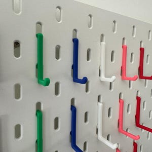 May include: A white pegboard with various colored hooks. The hooks are in different colors, including black, green, blue, white, pink, and red.