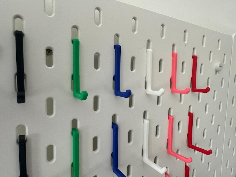 May include: A white pegboard with various colored hooks. The hooks are in different colors, including black, green, blue, white, pink, and red.