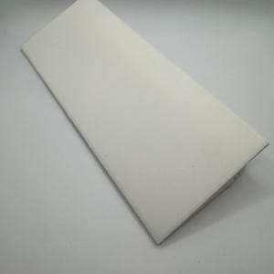 Puede incluir: Una pieza rectangular de pl&aacute;stico blanco con un borde biselado. El pl&aacute;stico es liso y parece estar hecho de un material duradero.