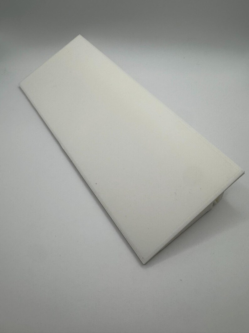 Puede incluir: Una pieza rectangular de pl&aacute;stico blanco con un borde biselado. El pl&aacute;stico es liso y parece estar hecho de un material duradero.