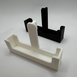 以下が含まれることがあります： 白と黒の2つの3Dプリントされたカードホルダーが白い背景に表示されています。各ホルダーは、中央に垂直のサポートと湾曲したエッジを備えた長方形のベースを持っています。