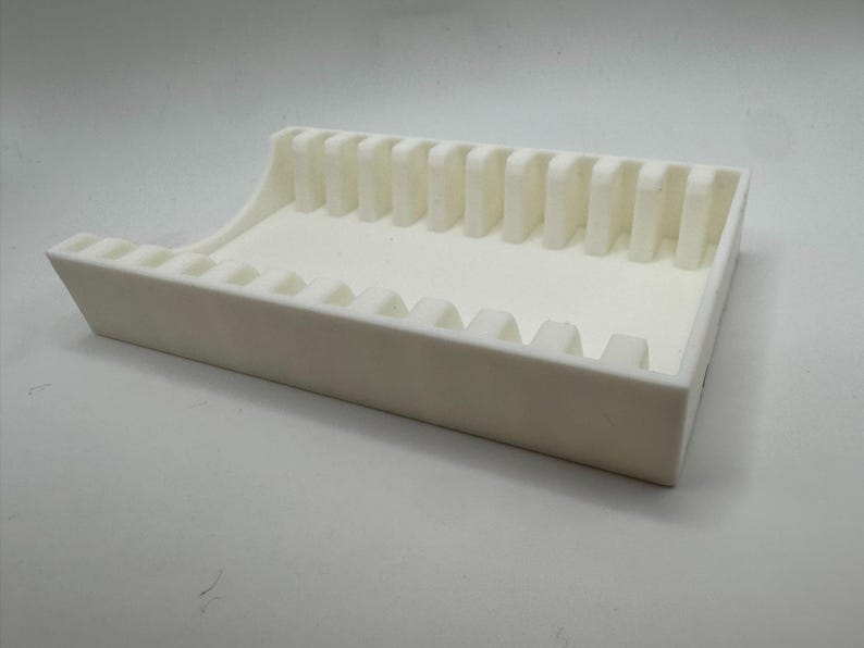 Op de afbeelding: Een witte, rechthoekige lade met verticale verdelers. De lade heeft een gebogen rand en is ontworpen om kleine items in te bewaren. Het object is gemaakt van een solide, ondoorzichtig materiaal. Afmetingen in centimeters.