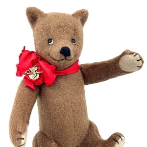 May include: A brown teddy bear with a red bow and a gold charm around its neck. The bear is sitting with its right arm outstretched.