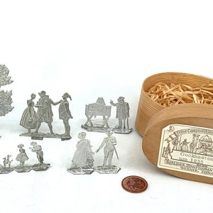 Puede incluir: Un conjunto de figuras de juguete de hojalata vintage en una caja de madera. Las figuras representan personas con ropa tradicional y un árbol. La caja está etiquetada "Guckkastenmann um 1835 (686)".
