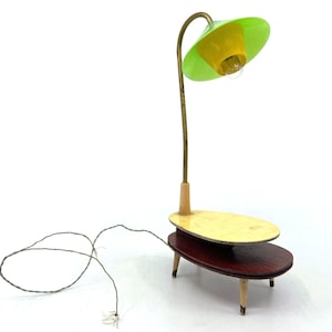 Könnte beinhalten: Eine moderne Tischlampe im Mid-Century-Stil mit einem grünen Lampenschirm und einem Holzsockel. Die Lampe hat ein Kabel und einen Schalter. Der Tisch ist aus Holz und hat eine hellbraune Oberfläche.