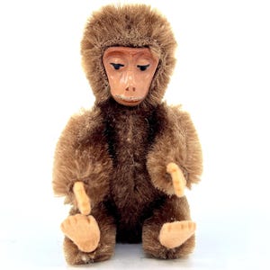 May include: A brown plush monkey toy with a brown face and a long, brown tail. The monkey is sitting with its arms crossed and its legs outstretched.