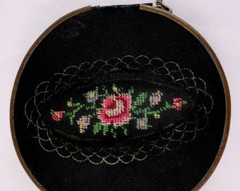 May include: A round black fabric coin purse with a gold zipper and a floral embroidery design. The embroidery features a pink rose with green leaves and pink, blue, and yellow flowers.