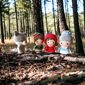 May include: Four crocheted stuffed toys in a woodland setting. A grey wolf, a girl in a red hooded cloak, a girl in a blue dress, and a boy in a green shirt and hat.
