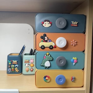 May include: Four colorful plastic storage boxes with different cartoon characters and the words "Toy Story" on the top box. Each box has a round knob for opening and closing.