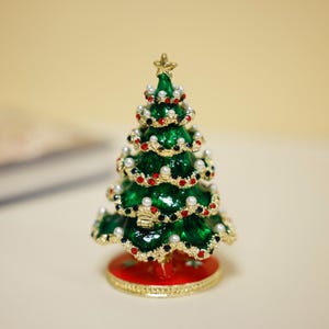 Op de afbeelding: Een klein, groen kerstboom ornament met rode en witte versieringen. De boom is gemaakt van metaal en heeft een gouden basis.