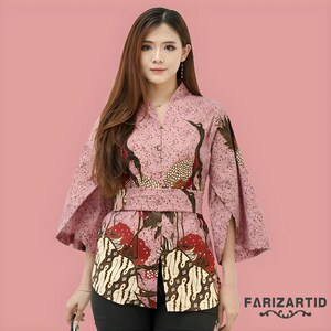 Könnte beinhalten: Ein rosa Kimono-Top mit passendem Gürtel. Das Oberteil hat ein Kranich-Design in Schwarz, Braun und Rot. Der untere Teil des Oberteils hat ein Batikmuster in Weiß und Braun. Der Text "FARIZARTID" ist unten rechts sichtbar.