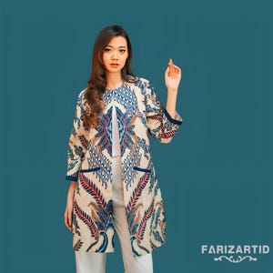 May include: A long-sleeved beige jacket with a blue and white batik pattern. The jacket has a collar and a front closure. The model is wearing white pants.