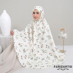May include: Cream-colored prayer garment with a floral pattern in shades of pink, gray, and brown. The fabric has a scalloped edge. A matching head covering is also visible. The text "FARIZARTID" is printed on the fabric.