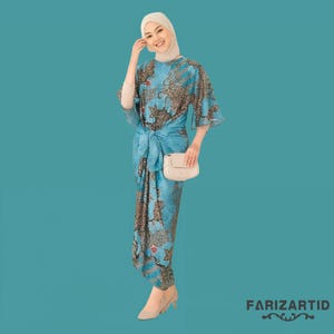 Könnte beinhalten: Eine Frau in einem blauen und braunen gemusterten Kleid mit einem weißen Kopftuch und einer weißen Handtasche. Das Kleid hat einen Knoten in der Taille und die Frau lächelt.