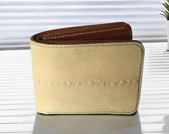 May include: A light beige leather wallet with a brown leather trim. The wallet has a textured surface and a stitched design.