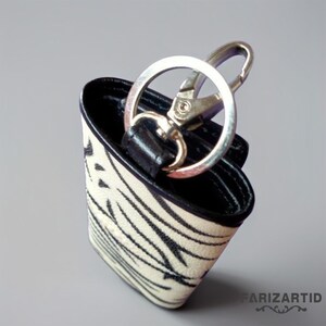 May include: A black and white zebra print leather key chain with a silver metal key ring and a silver metal clip.