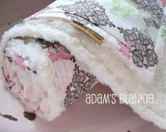 May include: A white faux fur baby blanket with a brown and pink floral print. The blanket is rolled up and has a tag that says "Adam's Blankie".