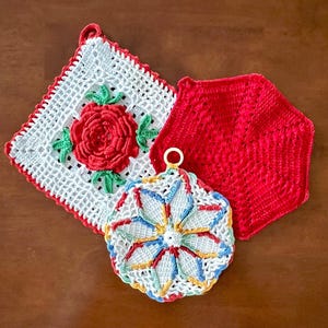 May include: Three handmade crochet pot holders. One is white with a red rose and green leaves, another is red and hexagonal, and the third is round with a starburst design in multiple colors.