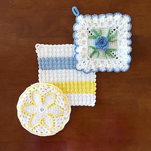 May include: Three handmade crochet items: a square potholder with a blue flower, a striped potholder with blue and yellow stripes, and a round coaster with a yellow flower design. All items are white with colorful accents.