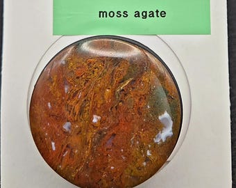 May include: A Rock Popup phone holder and stand featuring a moss agate stone. The holder is round, with a mix of brown, red, and white colors. The packaging includes the text "ROCK popup" and "Phone Holder and Stand."