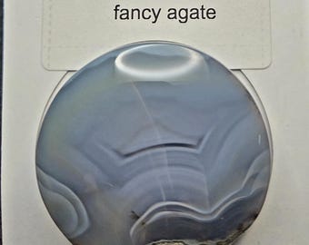 May include: A Rock Popup phone holder and stand with a fancy agate design. The holder is round and features a blue, gray, and white patterned stone. The packaging includes the text "ROCK popup" and "Phone Holder and Stand".