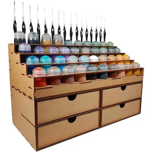 Peut inclure: Un organisateur de rangement en bois à plusieurs niveaux avec des découpes circulaires pour des pots de peinture et des pinceaux. L'unité comprend quatre tiroirs avec des poignées circulaires, en bois composite brun clair avec des joints visibles.