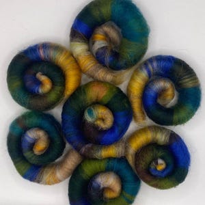 May include: Seven colorful hand-spun yarn balls in shades of blue, green, yellow, and brown. The yarn is arranged in a circular pattern, with each ball overlapping the next.