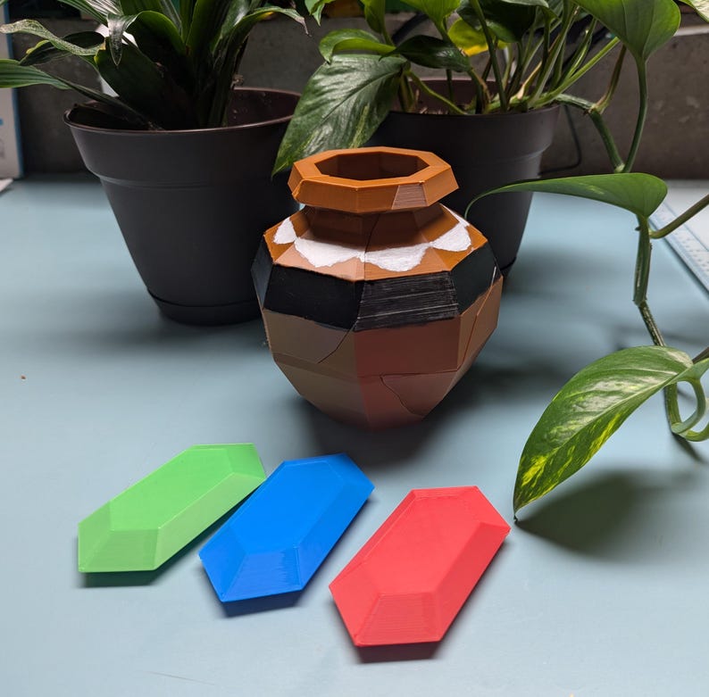 A clay pot with cracks in it, like it can be broken. Three crystal rupees, one red, one green, one blue.