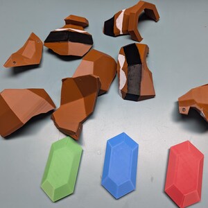 May include: A set of brown plastic pieces, possibly for a model or toy, along with three differently coloured gems. The gems are green, blue, and red.