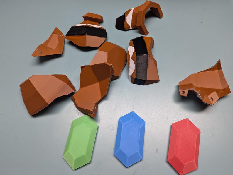 May include: A set of brown plastic pieces, possibly for a model or toy, along with three differently coloured gems. The gems are green, blue, and red.