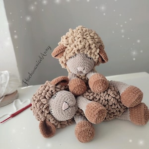 Puede incluir: Dos ovejas de ganchillo hechas a mano. Las ovejas son de color beige, beige claro y marrón claro. Las ovejas están tumbadas sobre una superficie blanca. Las ovejas tienen un aspecto suave y texturizado. El texto "HacovaniodAnny" está en la esquina superior izquierda.