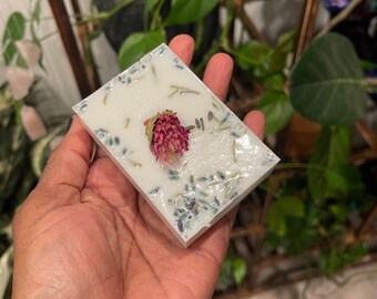 May include: A white soap bar with dried lavender and a pink flower embedded in it.