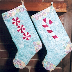 Pode incluir: Duas meias de Natal azuis com desenhos de bengala e menta. As meias têm um fundo branco com um padrão de redemoinho azul e são adornadas com um padrão de redemoinho e estrelas coloridas.