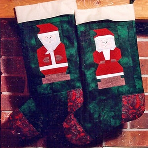 May include: Two green and red Christmas stockings with a white cuff. Each stocking features a patchwork design and a felt applique of Santa Claus with a white beard.