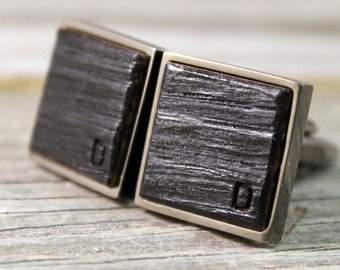 May include: A pair of square cufflinks featuring dark, textured wood inlays set within polished silver-toned metal frames. Each wooden face displays a small, subtle letter D engraved into the lower corner, showcasing a distinct grain pattern.