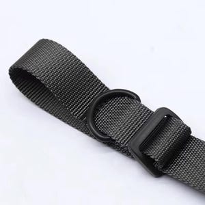 May include: Close-up of a black nylon strap with a D-ring and a square buckle. The strap is a dark gray color and has a woven texture. The hardware is black. The image is set against a white background.