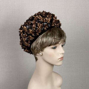 Puede incluir: Un sombrero marrón y negro con un diseño único y texturizado. El sombrero está hecho de tela y tiene una forma redondeada. Lo lleva puesto un maniquí con el pelo corto y castaño.