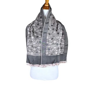 Peut inclure: Une écharpe à motifs gris et blancs avec une bordure à franges. L'écharpe est présentée sur un mannequin blanc.