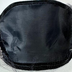 May include: A black hat with a rounded crown and a black veil. The hat is trimmed with small, silver-colored beads. The interior of the hat is lined with a black fabric.