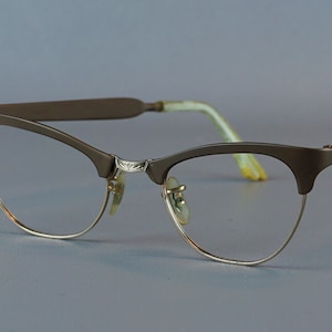 Op de afbeelding: Een paar bruine cat-eye brillen met gouden metalen monturen en heldere glazen.