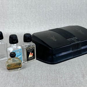 May include: A black plastic vanity case with a hinged lid, containing four small glass bottles with black caps. The bottles are labelled "Cutex Cuticle Oil" and "Cutex Remover".