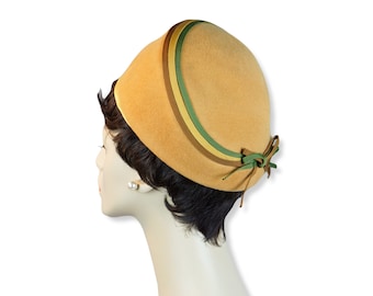 May include: A tan felt hat with a wide brim and a green, brown, and yellow ribbon around the crown. The ribbon is tied into a bow at the back of the hat.