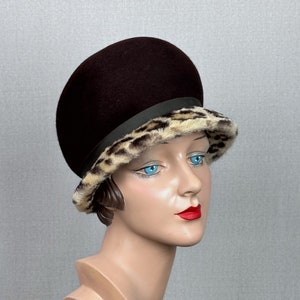 May include: A brown felt hat with a leopard print trim. The hat has a wide brim and is tilted slightly to the side.