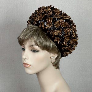 May include: A brown and black hat with a large, fluffy, round crown. The hat is made of a woven material and has a slightly textured surface.