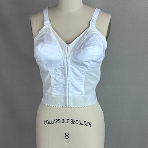 Könnte beinhalten: Weißer BH mit Reißverschluss vorne und verstellbaren Trägern. Der BH hat einen Spitzenbesatz am Saum und die Worte "Collapsible Shoulder" und die Zahl "8" sind auf dem Mannequin aufgedruckt.