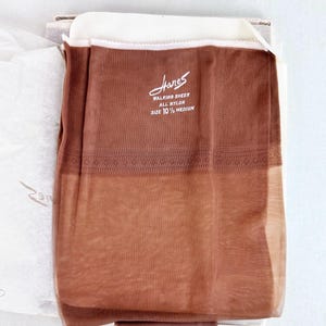 Pode incluir: Um par de meias de nylon Hanes Walking Sheer, tamanho 10 1/2 médio. As meias são de cor castanho claro e ainda estão na embalagem original. A embalagem inclui o logótipo Hanes e informações sobre o produto.